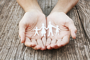 Estate planning hands holding cutout paper family on wood background